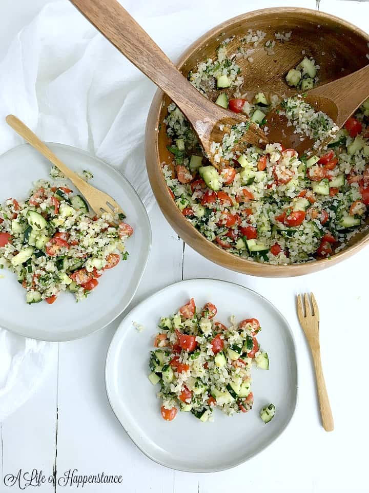 A brown bowl filled with cauliflower tabbouleh and two white plates with tabbouleh. 