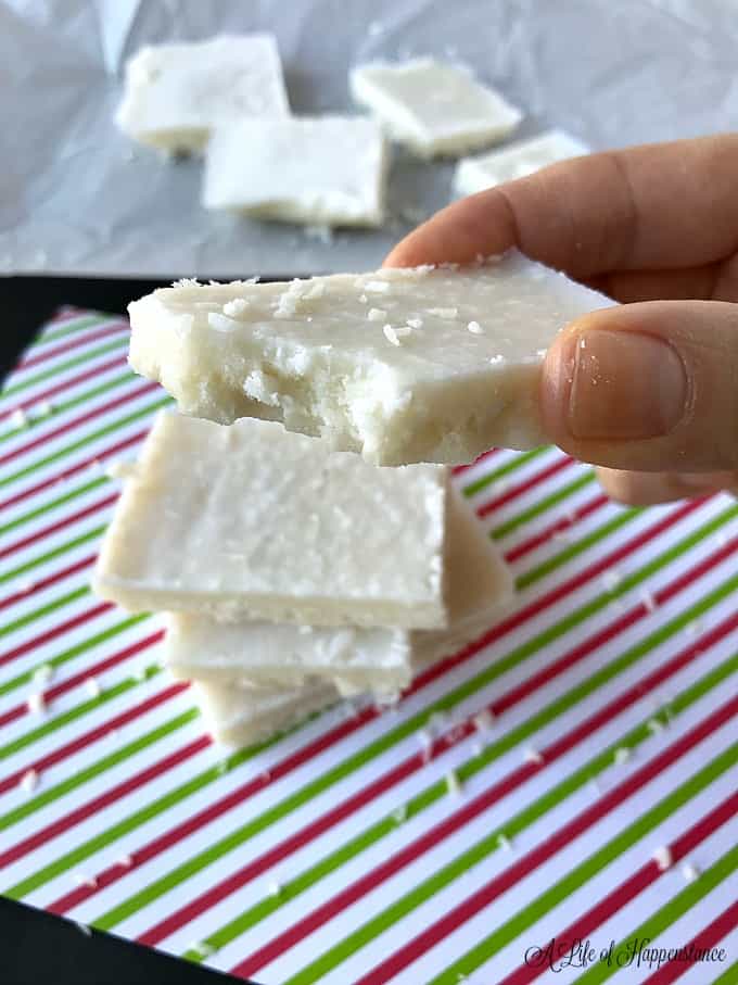 Holding a piece of coconut fudge with a bite taken out of it. 