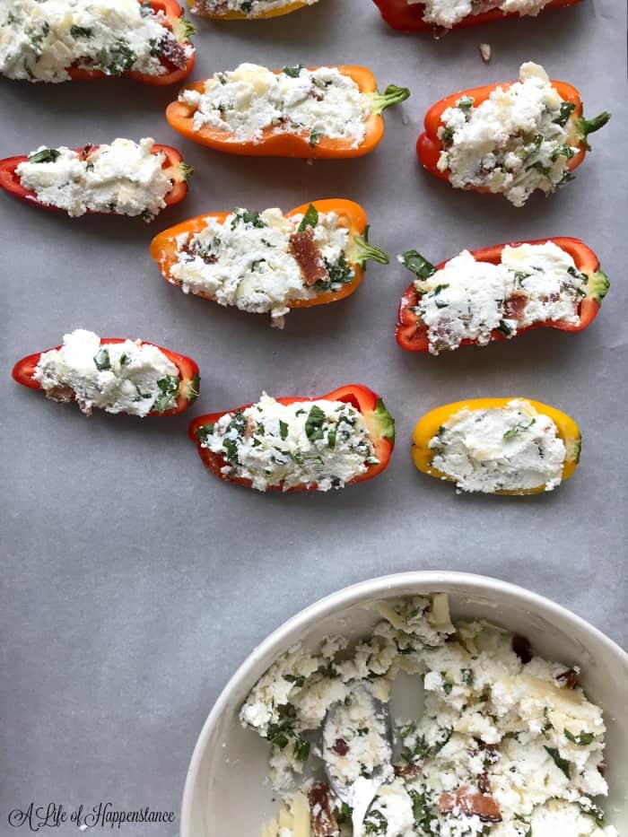 Mini peppers filled with cheese mixture on a parchment lined baking sheet. 