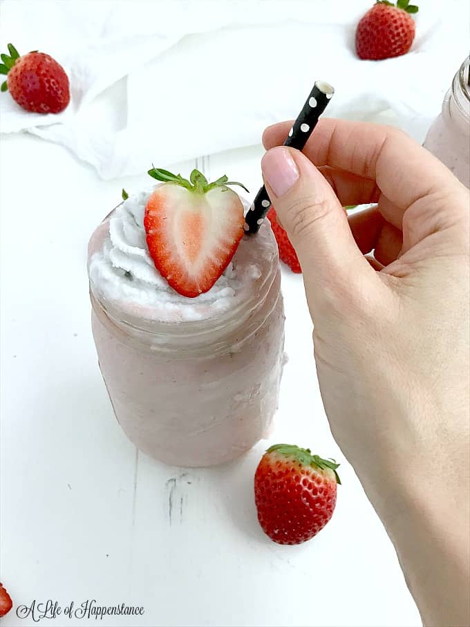 A mason jar filled with strawberry shortcake smoothie and garnished with whipped coconut cream and a strawberry. 