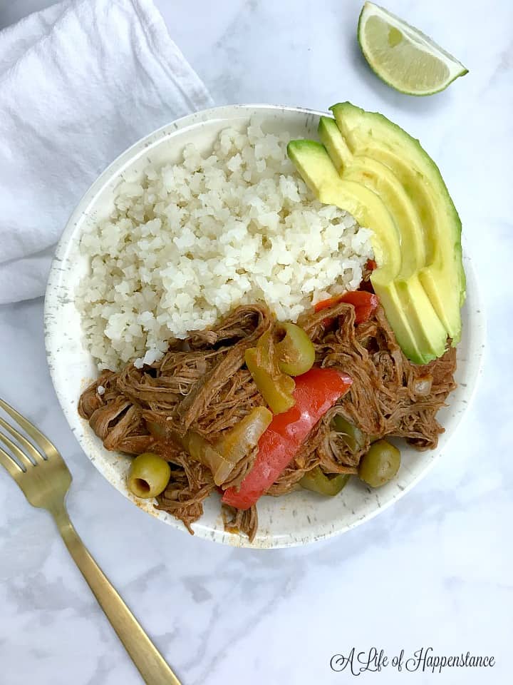 Cuban ropa vieja in a bowl along with cauliflower rice and sliced avocado. 