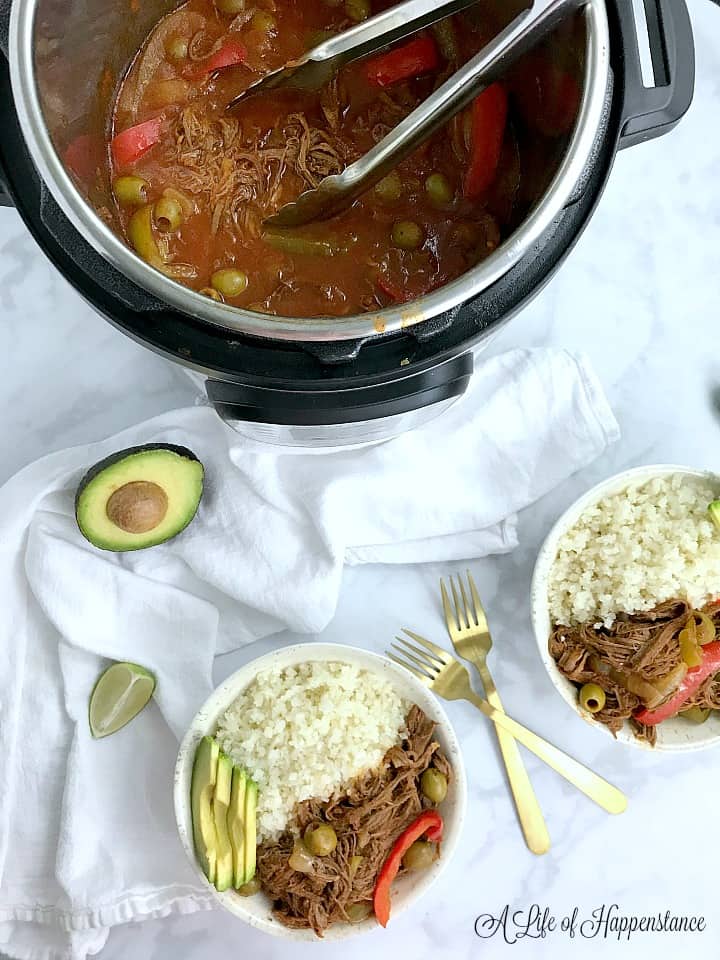 Two bowls filled with ropa vieja, cauliflower rice, and avocado with the rest of the beef in the Instant Pot. 