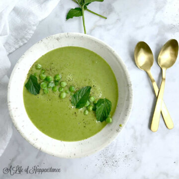 A white bowl filled with mint pea soup and garnished with fresh peas and mint leaves.