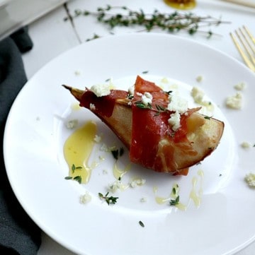 A pear slice on wrapped in a piece of prosciutto and drizzled with honey and crumbled cheese.