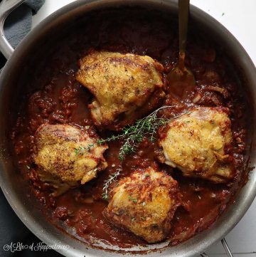 Italian braised chicken thighs sitting on top of a red sauce in a large saute pan.