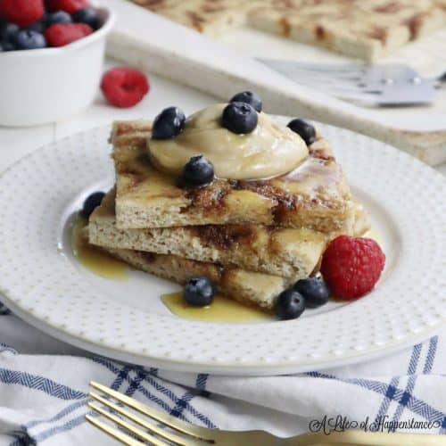 Three sheet pan pancakes on a white plate topped with cashew cream, honey, and berries.