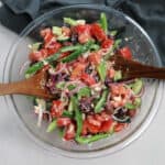 The salad in a glass bowl with wooden serving utensils.