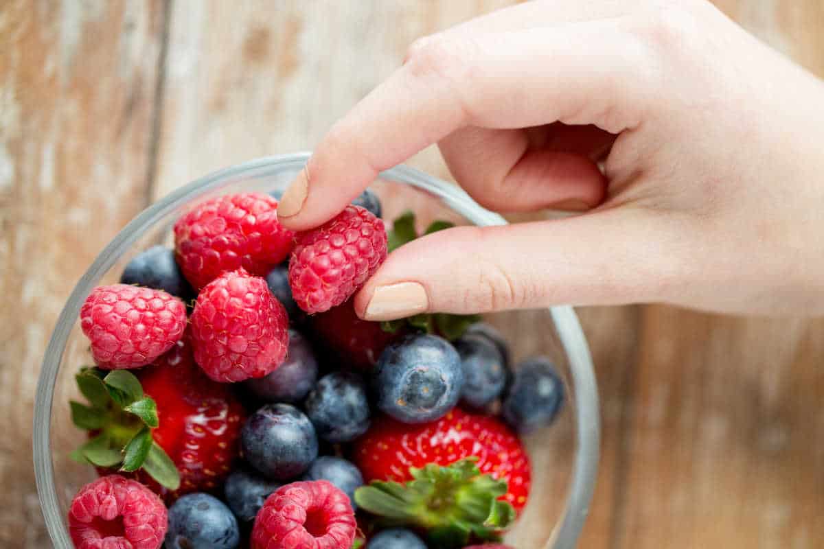 A hand picking a raspberry out of a bowl.