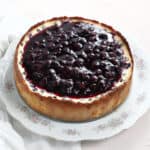 A cheesecake removed from the pan and cooling on a serving platter.