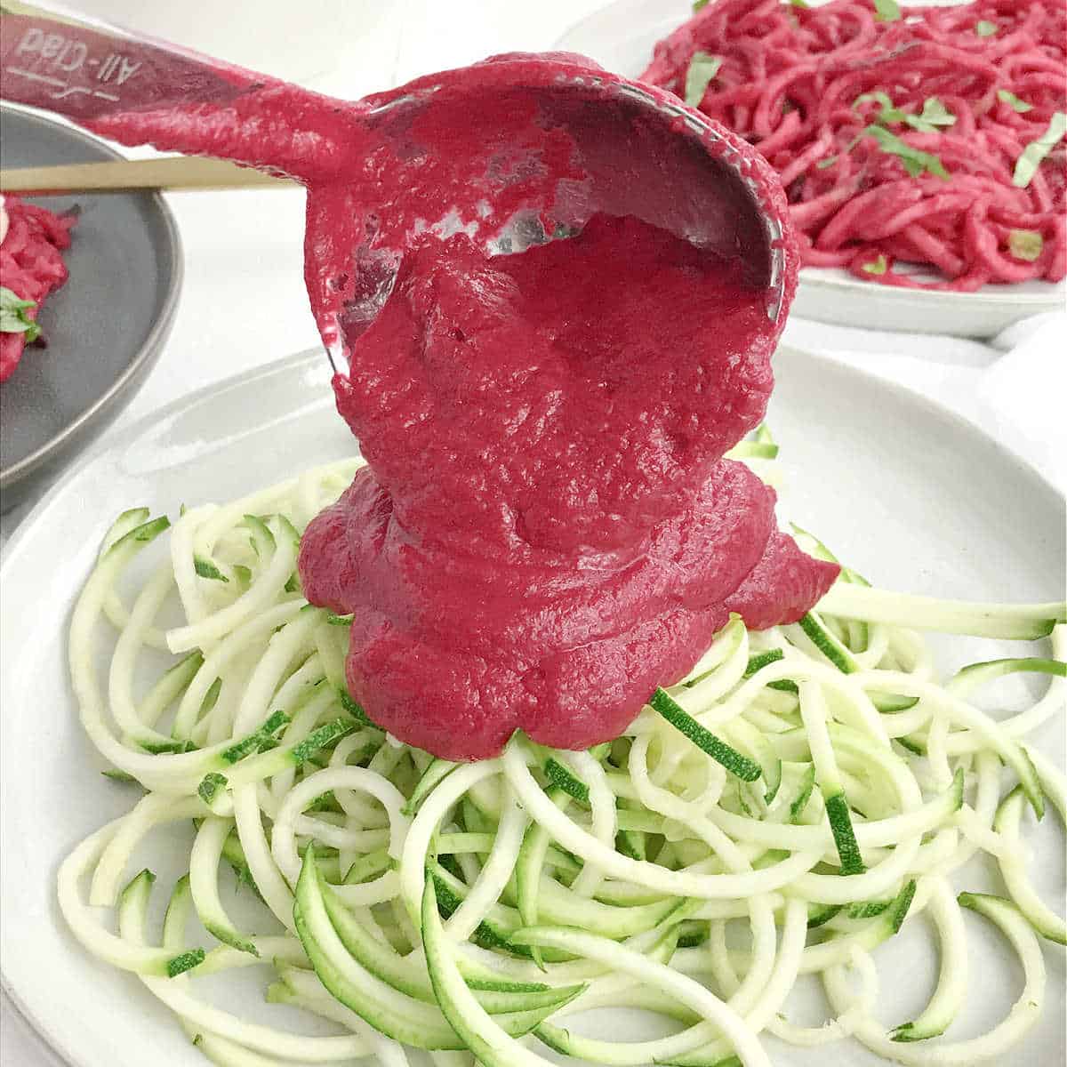 Ladling sauce onto a plate of zucchini pasta.