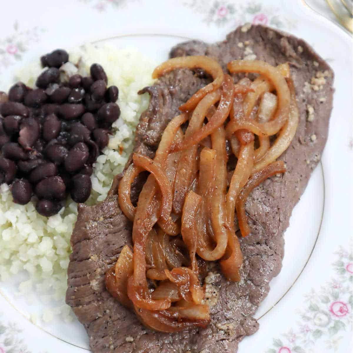 Black beans, cauliflower rice, and Cuban steak with onions on a white plate.