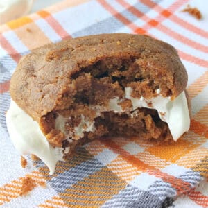 A whoopie pie with a bite taken out of it on a plaid napkin.