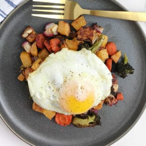 Roasted veggies topped with an egg on a black dish.