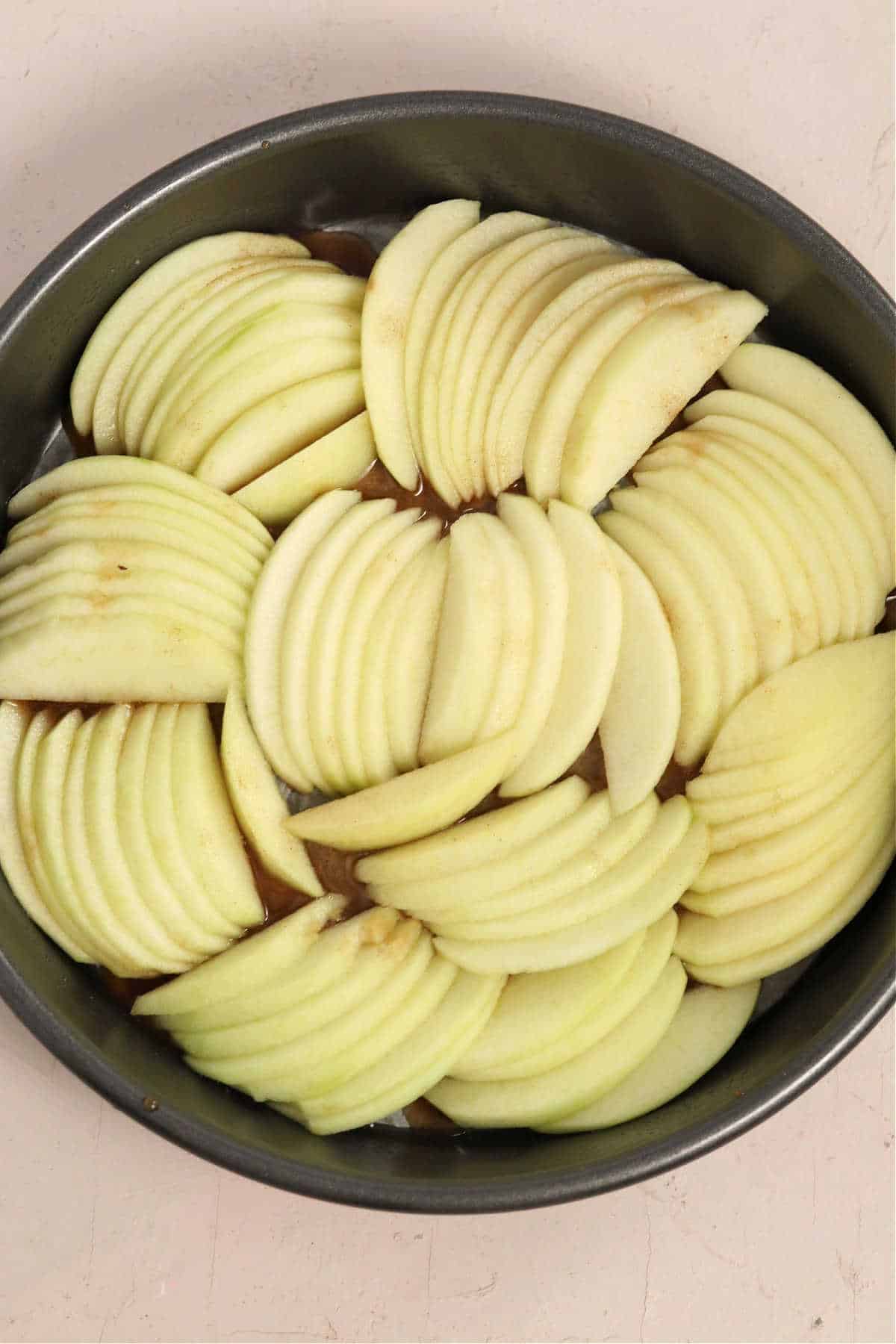 Peeled and thinly sliced apples arranged in a cake pan.